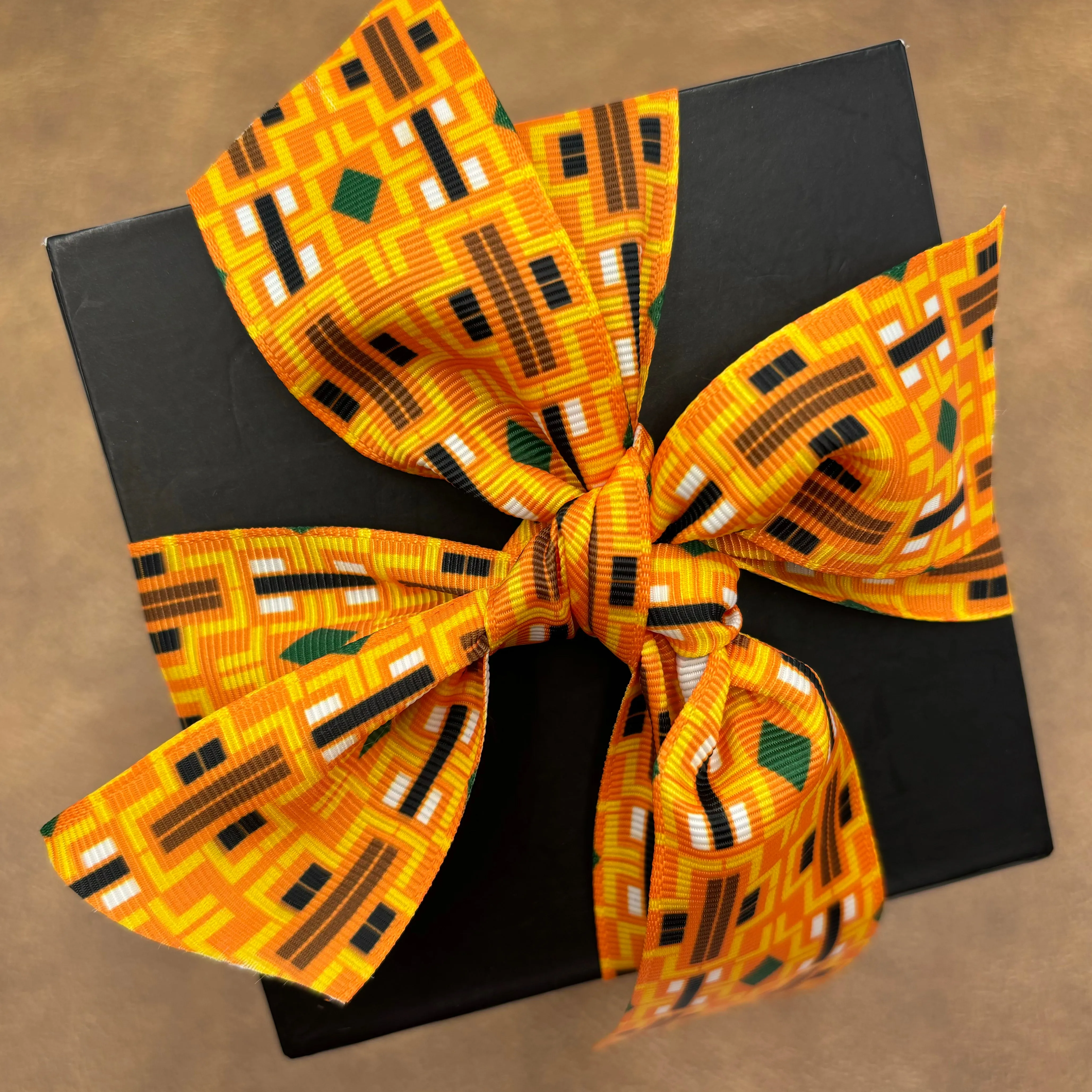 Aztec Design ribbon printed in three color ways of orange, black and cream printed on 1.5" white grosgrain